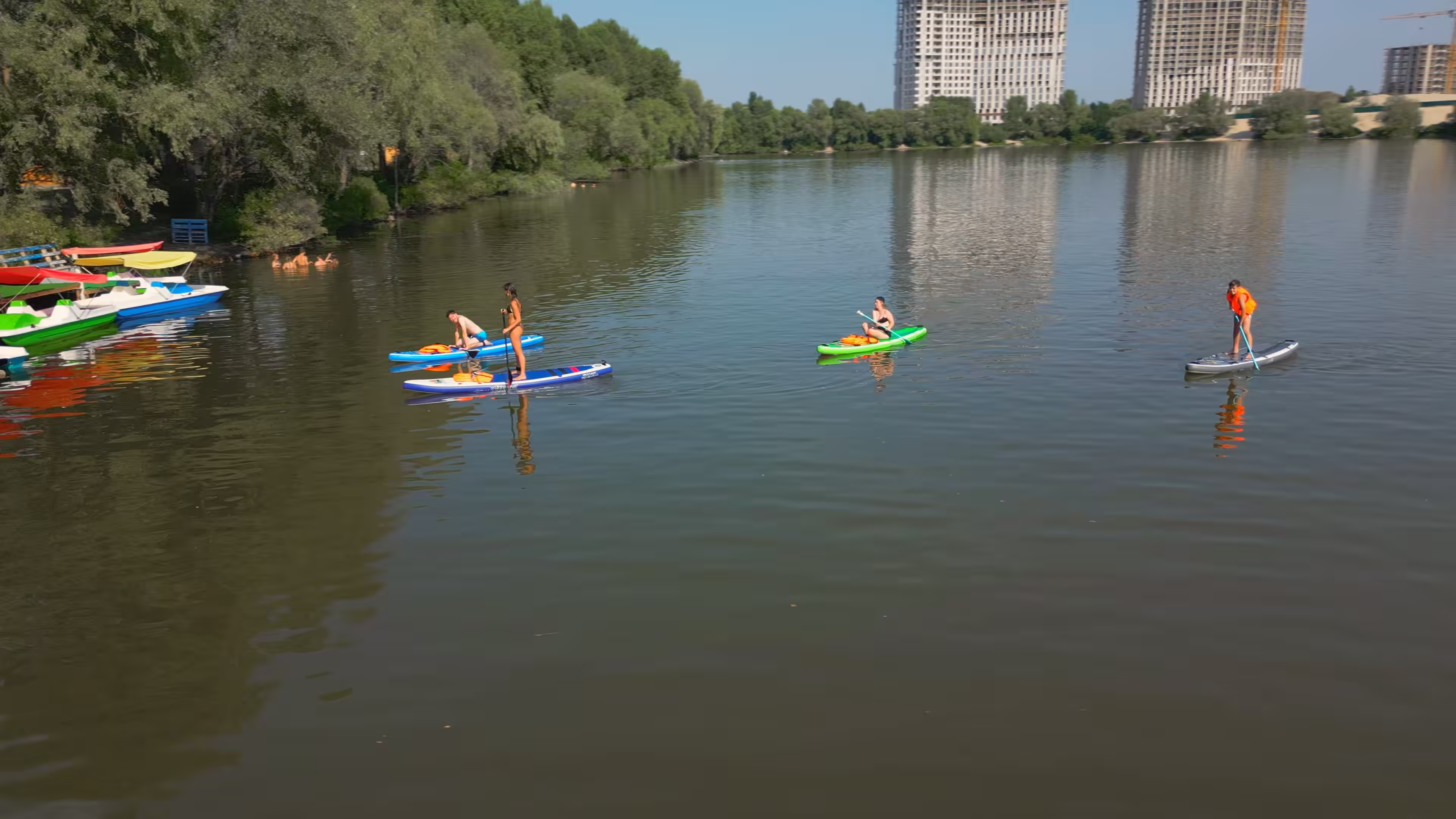 Стоп-кадр із фонового відео для сайту комплексу Небреж Віледж: комбінована зйомка з землі та дрона, що демонструє вейкбординг, сапборди, альтанки та літній відпочинок біля озера — Добре Кіно Київ